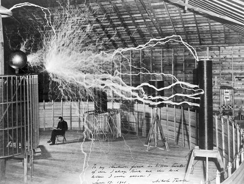 Nikola Tesla in his lab seated under bolts of electricity